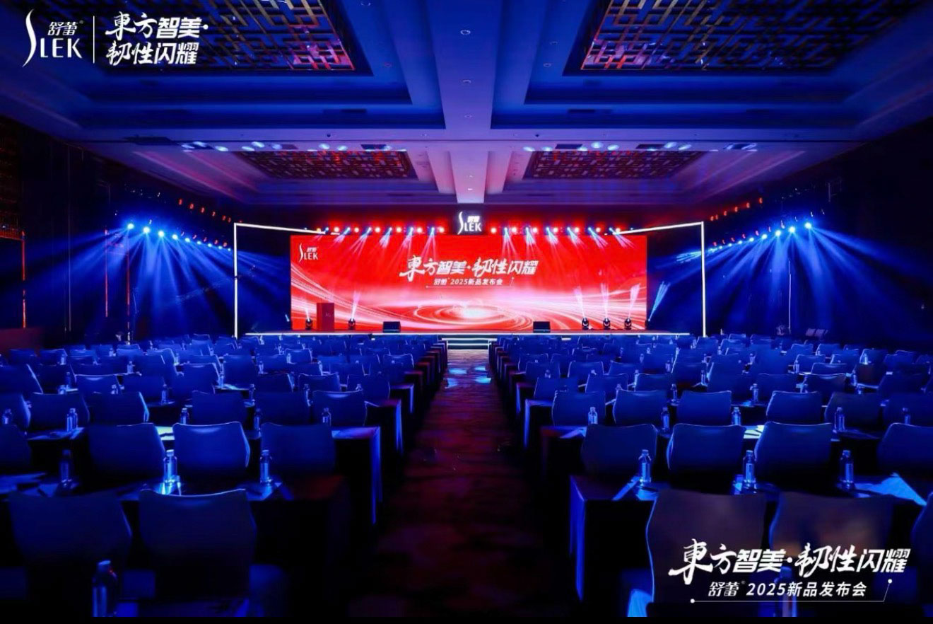 企业新品发布会会场，蓝红舞台灯光照亮品牌主屏和观众席